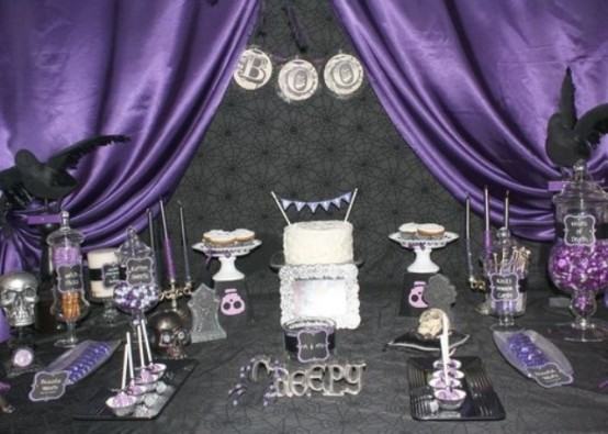 a black and purple Halloween party sweet table with various candies, cupcakes and other sweets, with purple curtains over it is a very dramatic decor idea