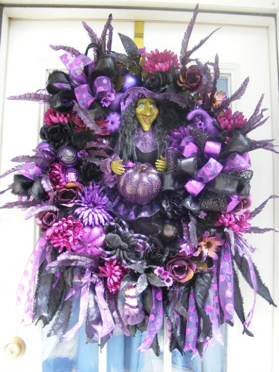 a very catchy and complicated looking Halloween wreath with feathers, ornaments, a witch, faux blooms, ribbons, bows and much, much more