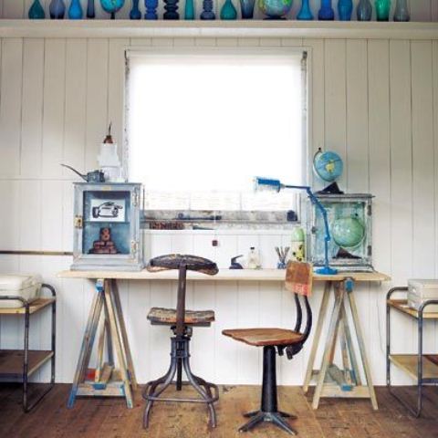 a rustic coastal home office wiht white walls, a trestle desk, industrial chairs and some blue bottles and vases for decorating