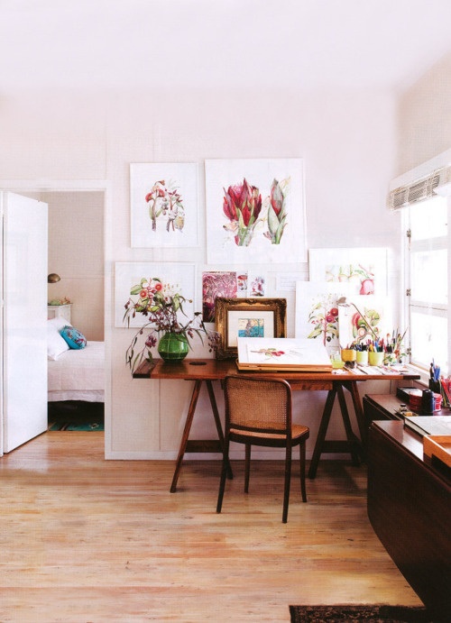 a vintage rustic home office with a trestle desk, dark tables and a bright gallery wall with flower art works