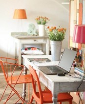 a bright rustic home office with wooden desks, bright orange and pink lamps and potted blooms and some artworks