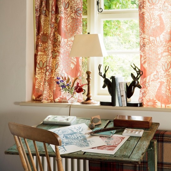 a bright rustic home office with colorful curtains, a shabby chic desk, wooden chairs, a table lamp and some decor