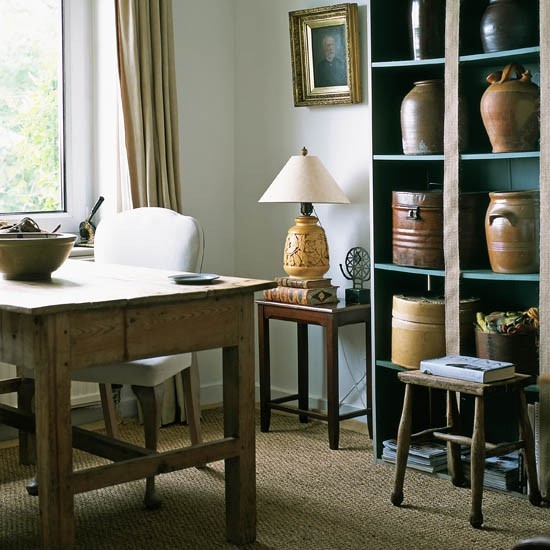 a refined rustic home office with a blue shelving unit, a rustic wooden desk, some lamps and artworks