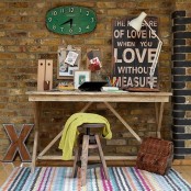 a rustic industrial home office done with an exposed brick wall, a wooden desk, a colorful striped rug and a clock and a sign