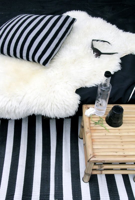 a Scandinavian balcony with a black and white striped rug and a pillow, faux fur and a stained side table