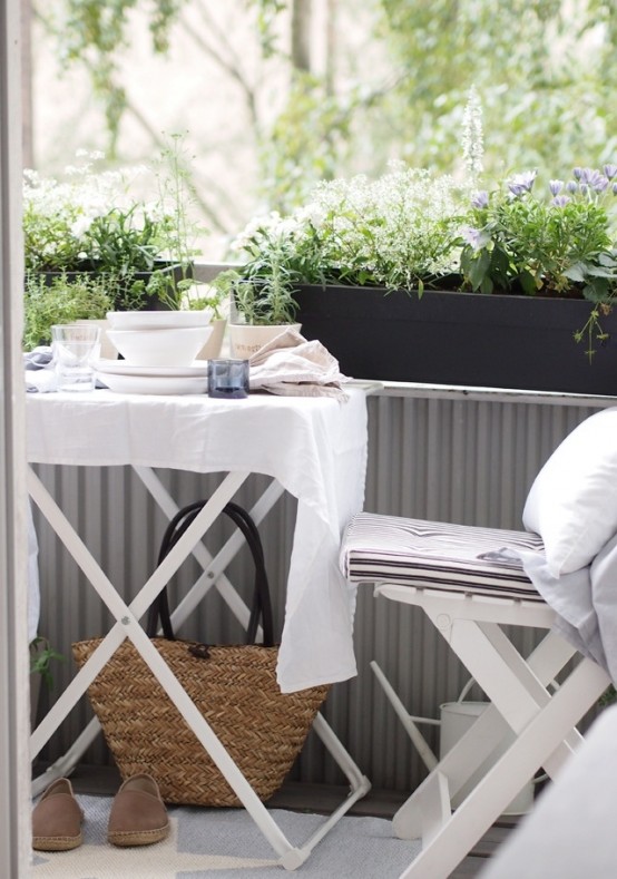 a Scandinavian balcony with white folding garden furniture, black planters with greenery and blooms and white textiles is a lovely idea