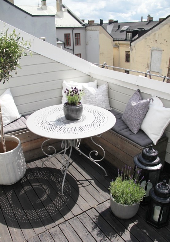 a cool Scandinavian balcony with a corner sofa with pillows and cushions, candle lanterns, potted blooms and greenery and a white table