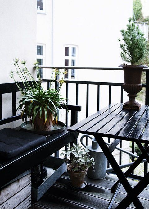 a Nordic balcony in black, with simple wooden furniture, potted greenery and blooms is a stylish idea for those who love moody colors