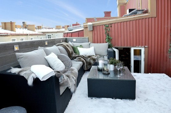 a Nordic balcony with a black wicker sofa and a black coffee table, grey and white pillows and blankets is a chic and cool idea