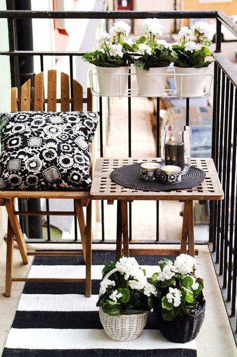 a Scandinavian balcony with stained furniture, black and white textiles and black and white planters and pots with blooms is a stylish idea