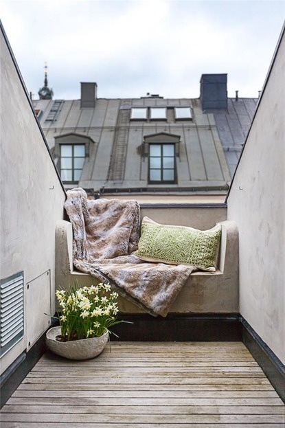 a very small Scandinavian balcony with a built-in seat with pillows and a blanket, potted blooms is a simple and chic space to stay