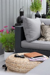 a Nordic balcony with grey and black furniture and grey upholstery, jute poufs, potted greenery and blooms and candle lanterns in Moroccan style