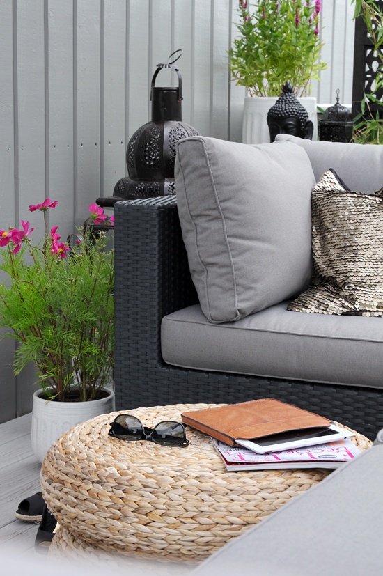 a Nordic balcony with grey and black furniture and grey upholstery, jute poufs, potted greenery and blooms and candle lanterns in Moroccan style