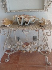 a refined sea-inspired console table with lots of seashells covering it and with seashells on top for a beach entryway
