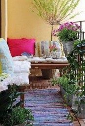 a bright boho terrace with potted blooms and greenery, a bench with colorful and patterned pillows and a rug