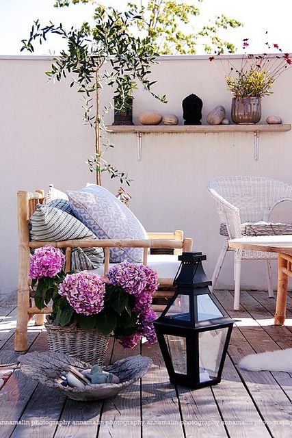 a tiny eclectic terrace with rattan and wicker furniture, candle lanterns and potted greenery and blooms