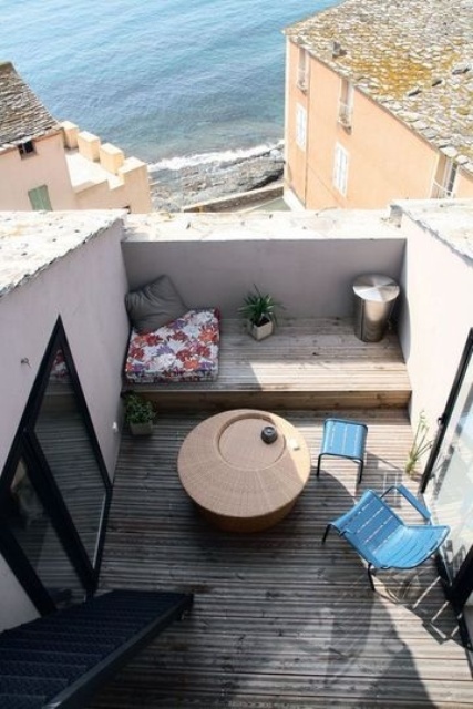 a small terrace with a beach view, blue chairs, a wicker table and a bright pillow plus a smaller one