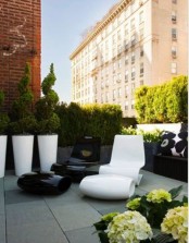 a minimalist monochromatic terrace with potted greenery and flowers, a whimsical black and white chair, large white planters