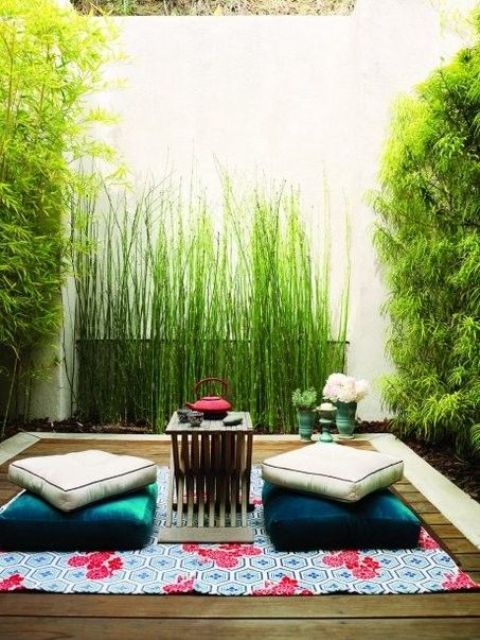 a small zen terrace with a rug, cushions and a tiny coffee table and lots of greenery and bamboo around