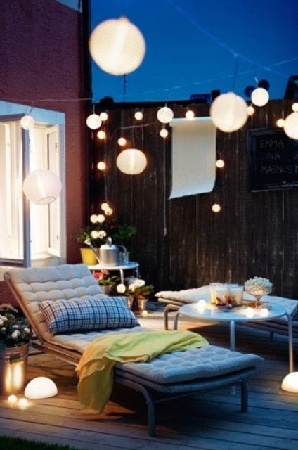a small terrace with comfy contemporary furniture, lights, blooms and greenery in pots