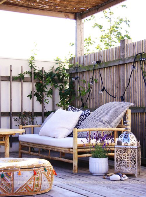 a small boho terrace with candle lanterns, rattan furniture, potted greenery and blooms plus lights