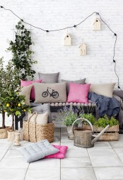 a small colorful terrace with a bench and bright pillows, potted greenery and blooms plus lights