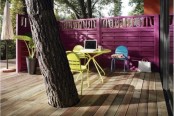 a small bright terrace with a fuchsia wall, bright yellow furniture, a blue chair and a comfy working space