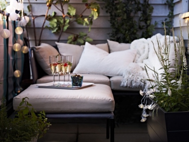 a small contemporary terrace with potted greenery, neutral upholstered furniture and lights