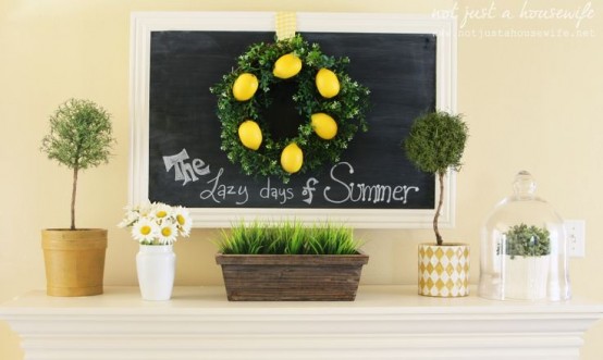 a traditional summer mantel with a chalkboard, a lemon wreath, potted blooms and greenery and a box with grass