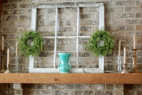 a simple rustic summer mantel with a vintage window, greenery wreaths, candles and a turquoise vase
