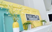 a colorful summer mantel in turquoise and yellow, with potted greenery, a sign and blooming branches