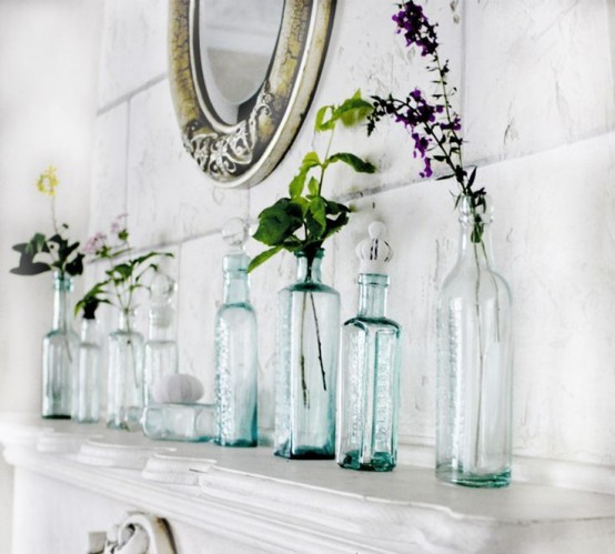a white mantel with bottles and vases with some blooms and greenery