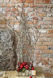 frozen branches tucked into a moss pillow decorated with red ornaments and wrapped with bark is a stylish alternative to a usual tabletop Christmas tree
