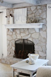 a whitewashed stone fireplace with large pinecones, a white mantel with antlers and pinecones for a strong rustic touch