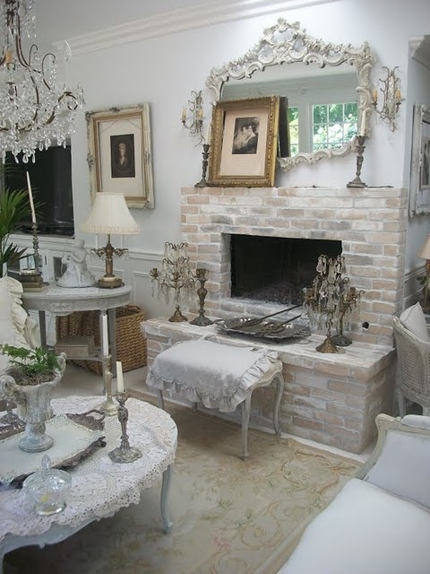 a very delicate and refined vintage interior with a whitewashed fireplace, with a mantel with artworks and a vintage frame mirror