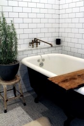 a Scandinavian bathroom with white subway tiles, a black vintage tub and a potted plant for enlivening the space at once