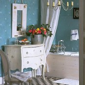 a vintage-inspired bathroom with blue wallpaper walls, refined white furniture and some blooms in a bucket planter for a rustic feel