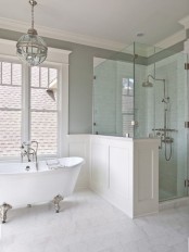 a chic neutral farmhouse bathroom with grey walls and white paneling, pon walls in the shower space and a vintage bathtub and a chandelier