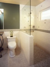 a catchy bathroom with a black wall, neutral tiles cladding the shower space and a half wall with a glass space divider