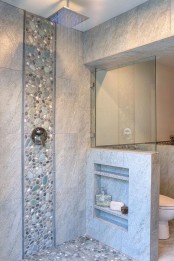 a neutral bathroom clad with tiles and faux pebbles, with a pony wall that had some shelves integrated is a lovely space