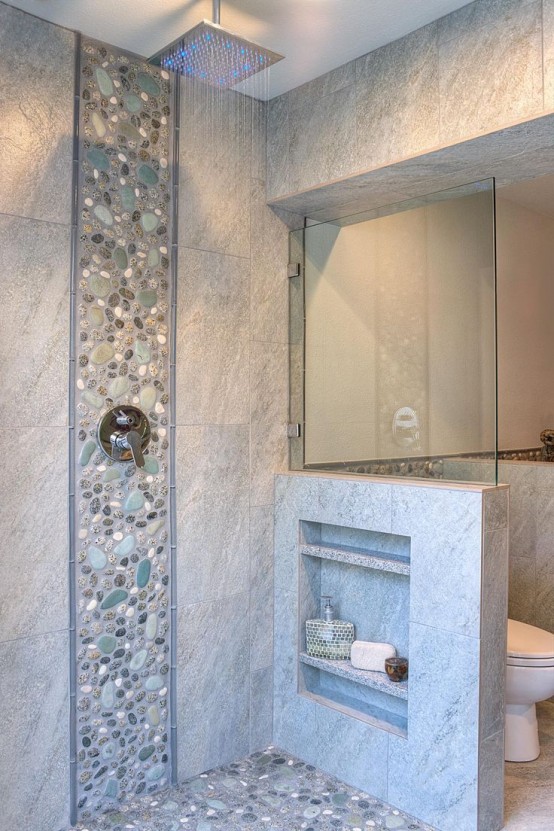 a neutral bathroom clad with tiles and faux pebbles, with a pony wall that had some shelves integrated is a lovely space