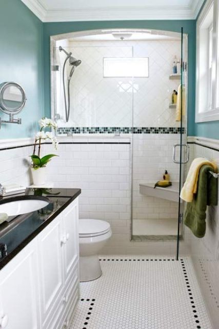 a small neutral bathroom with turquoise walls, white tiles all over, a half wall and a white and black vanity is chic