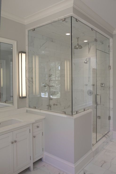 a refined bathroom with marble tiles on the walls, a shower space enclosed in glass and with white pony walls plus a large vanity