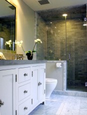 a chic bathroom with white walls, a shower space with a pony wall and grey tiles, a large white vanity with a grey stone countertop