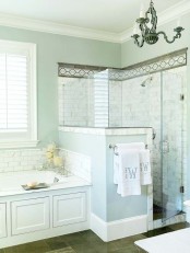 a light blue bathroom with a shower space clad with tiles, light blue walls and a half wall, a bathtub clad with panels