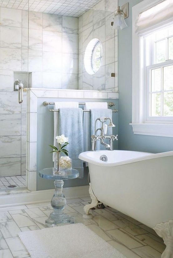 a beautiful bathroom with blue walls and a shower space clad with marble tiles, with a vintage bathtub and a pony wall in the shower space
