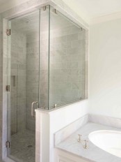 a neutral bathroom with a small shower space clad with tiles, a pony wall and a glass partition, a built-in sink in the vanity