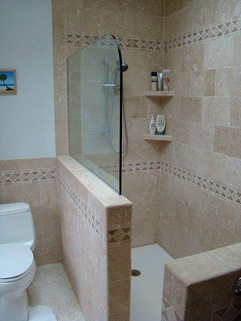 a sandy colored bathroom with a pony wall and a glass wall divider on it to separate the shower space from the rest of the room