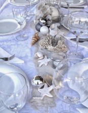 a silver and white beach Christmas tablescape with seashells, starfish, corals and neutral tableware and linens