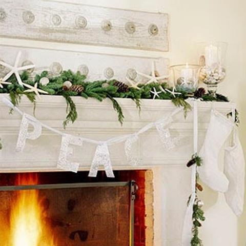 a beach Christmas mantel with evergreens, pinecones, starfish, glasses with seashells and pillar candles, a letter bunting, stockings